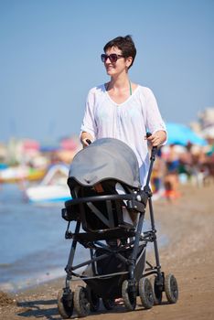 happy young mother walking on beach and push baby carriage