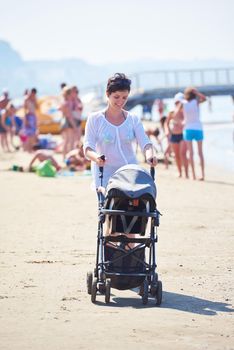 happy young mother walking on beach and push baby carriage