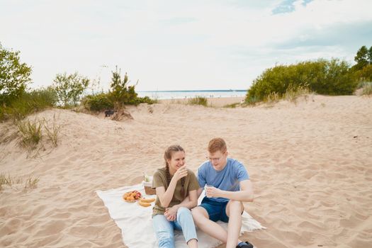 Picnic on beach with food and drinks. Young boy and girl sitting on sand. Teens couple. Sunny summer day, rest.
