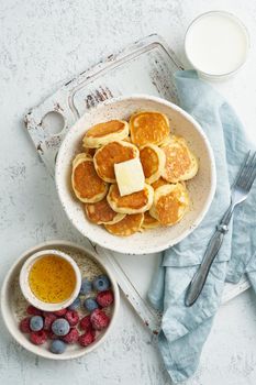 Pancakes cereal, trendy food, tiny thin funny crumpet, children's food. Breakfast with drink, white table, bright morning, top view, vertical