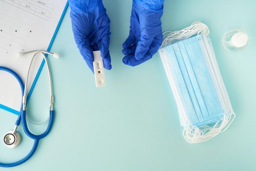 Negative test for antibodies to covid-19 virus. Bright blue table, medical mask, doctor's hands holding an express test for coronavirus
