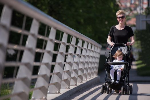 beautiful young mother with blond hair and sunglasses pushed her baby daughter in a stroller on a summer day