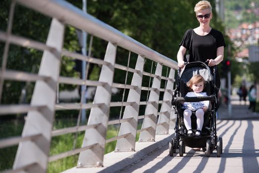 beautiful young mother with blond hair and sunglasses pushed her baby daughter in a stroller on a summer day