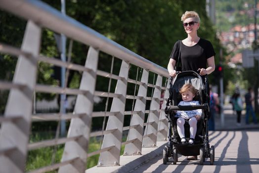 beautiful young mother with blond hair and sunglasses pushed her baby daughter in a stroller on a summer day