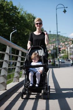 beautiful young mother with blond hair and sunglasses pushed her baby daughter in a stroller on a summer day