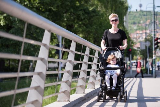 beautiful young mother with blond hair and sunglasses pushed her baby daughter in a stroller on a summer day