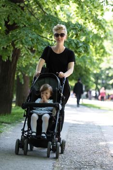 beautiful young mother with blond hair and sunglasses pushed her baby daughter in a stroller on a summer day