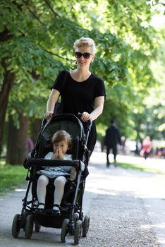 beautiful young mother with blond hair and sunglasses pushed her baby daughter in a stroller on a summer day