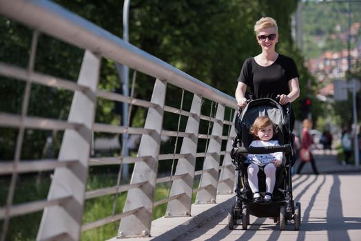 beautiful young mother with blond hair and sunglasses pushed her baby daughter in a stroller on a summer day