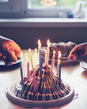 Hands with matches from above lighting nineteen candles on colorful sweet birthday dessert donuts on background vertical