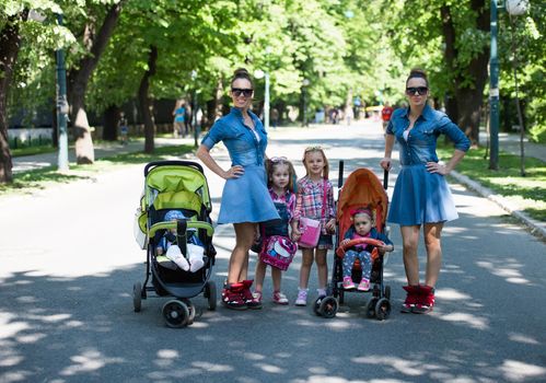 Young beautiful twins mother with children enjoying a sunny day in city park