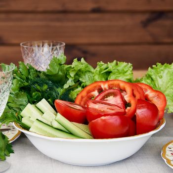 Bowl full of chopped fresh tomato, cucumber, pepper and lettuce healthy diet vegeterian food wooden wall and glassware on background
