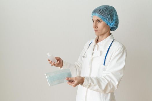 Female doctor in medical mask and uniform offers mask and disinfectant in bottle to prevent from coronavirus. Covid-19 protection, medical information. Copy space