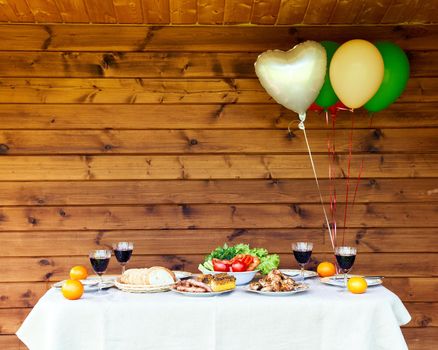 Festive table full of vegetables and fried bbq meat glasses full of drink with colorful air balloons on wooden background