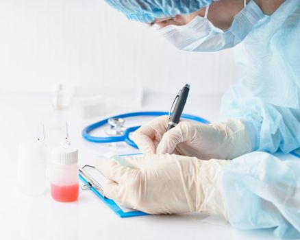 Pandemic COVID-19, Coronavirus. Doctor in hospital is on duty, avail for work, filling out forms. Woman in uniform and face mask conducts tests in laboratory, writes down results. Selective focus