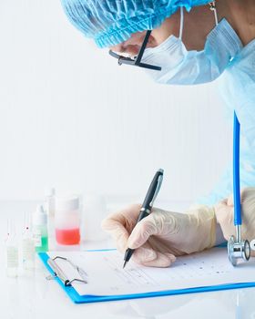 Pandemic COVID-19, Coronavirus. Doctor in hospital is on duty, avail for work, filling out forms. Woman in uniform and face mask conducts tests in laboratory, writes down results.