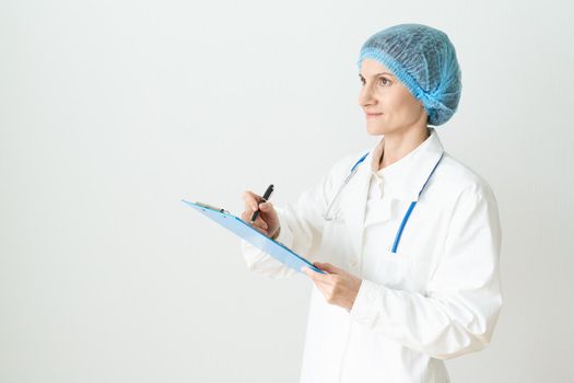 Female adult doctor stands on white background. Beautiful woman, thinking, smiling, writing. Clipboard in his hand, stethoscope around his neck .