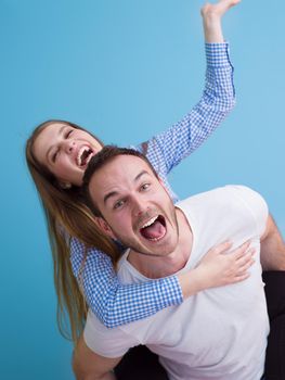 happy young man piggybacking his girlfriend isolated on blue background
