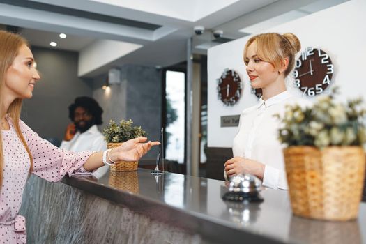 Blonde woman hotel guest checking-in at front desk in hotel close up