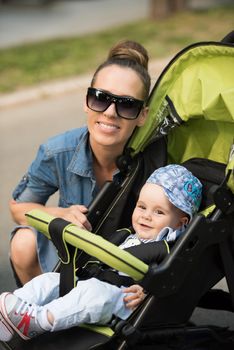 portrait of a beautiful young mother with sunglasses and a baby in a stroller on a sunny day in the park