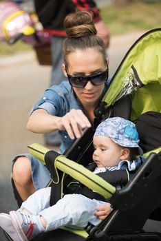 portrait of a beautiful young mother with sunglasses and a baby in a stroller on a sunny day in the park