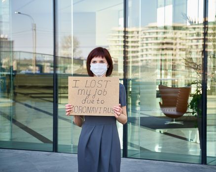 Woman in mask holds sign I lost my job because of coronavirus Concept of job loss due to COVID-19 virus pandemic. Female stands against background of business center