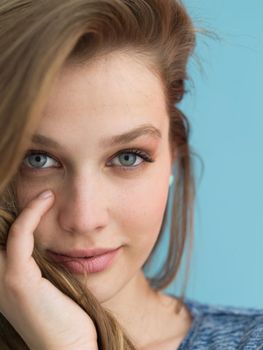 Portrait of a beautiful positive young woman while playing with her long silky hair isolated on blue background