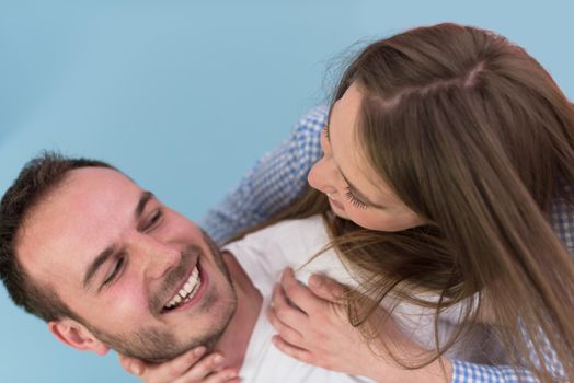 happy young man piggybacking his girlfriend isolated on blue background