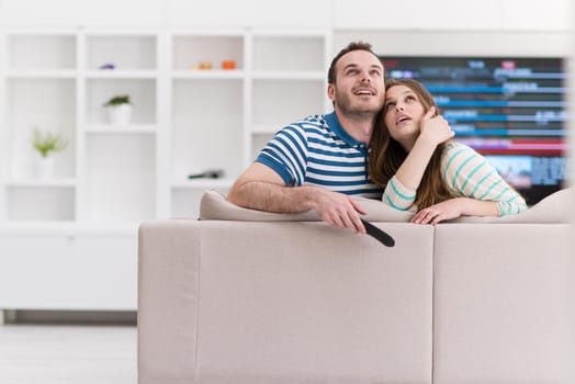 Young couple on the sofa watching television together in their luxury home