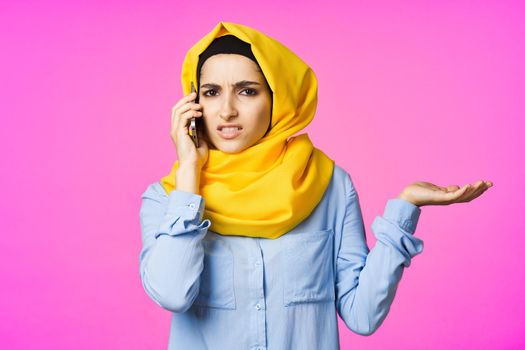 muslim woman in yellow hijab talking on the phone pink technology background. High quality photo
