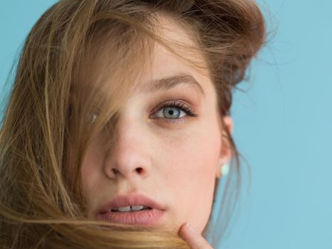 Portrait of a beautiful positive young woman while playing with her long silky hair isolated on blue background