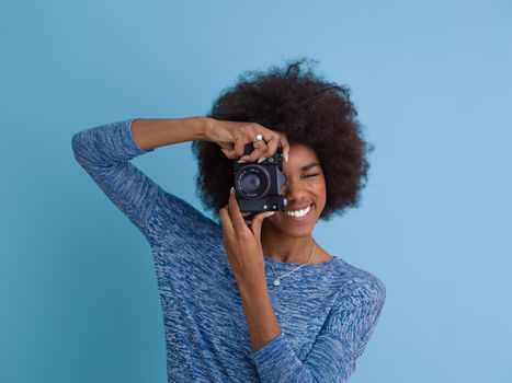 portrait of a smiling pretty african american girl taking photo on a retro camera isolated over blue background