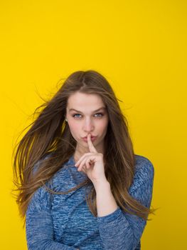 Portrait of a beautiful positive young woman while playing with her long silky hair isolated on yellow background
