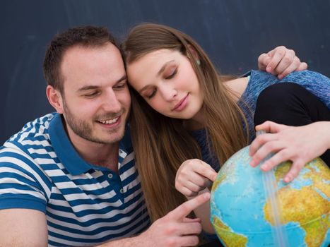 Young lovely couple in casual clothing investigating globe isolated over gray background