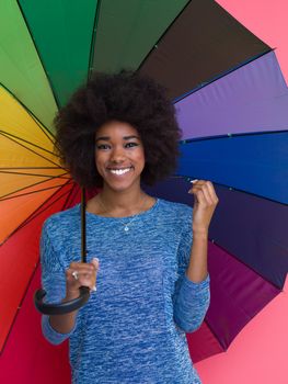 Portrait of young beautiful african american woman holding a colorful umbrella isolated on a Pink background