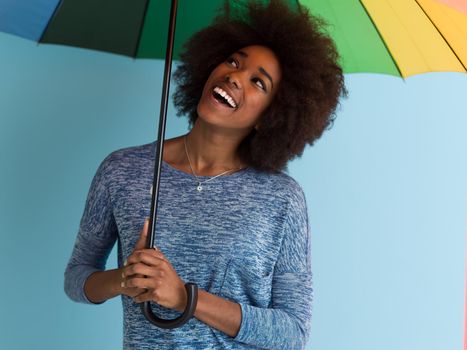 Portrait of young beautiful african american woman holding a colorful umbrella isolated on a Blue background