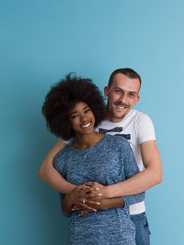 Young happy multiethnic couple laughing and hugging isolated on a blue background