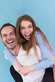 happy young man piggybacking his girlfriend isolated on blue background