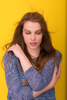 Portrait of a beautiful positive young woman while playing with her long silky hair isolated on yellow background