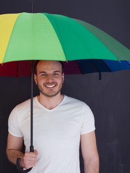portrait of a young handsome man with a colorful umbrella isolated on a gray background
