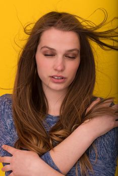 Portrait of a beautiful positive young woman while playing with her long silky hair isolated on yellow background