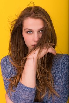Portrait of a beautiful positive young woman while playing with her long silky hair isolated on yellow background
