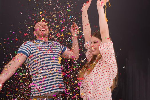 handsome young couple celebrating new year and chrismas party while blowing confetti decorations to camera isolated over gray background