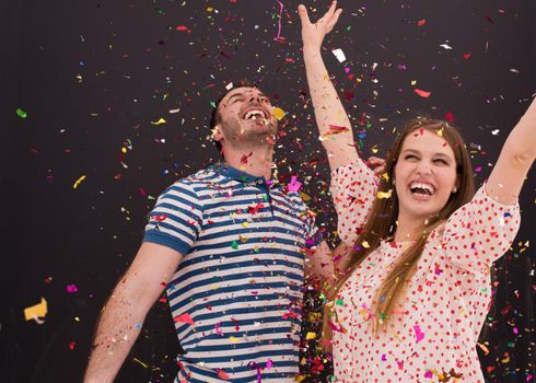 handsome young couple celebrating new year and chrismas party while blowing confetti decorations to camera isolated over gray background