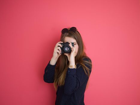 portrait of a smiling pretty girl taking photo on a retro camera isolated over red background