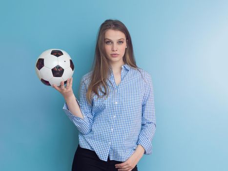 Portrait of a beautiful positive young woman while playing with a soccer ball isolated on blue background