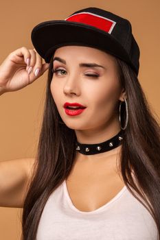 Hip-hop girl in cap with long dark hair. Fashion portrait of modern young woman in cap on beige background.