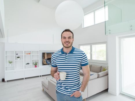 young handsome man drinking morning coffee by the window in his home