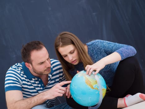 Young lovely couple in casual clothing investigating globe isolated over gray background