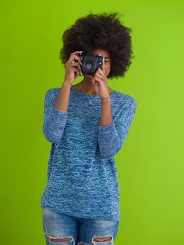 portrait of a smiling pretty african american girl taking photo on a retro camera isolated over green background